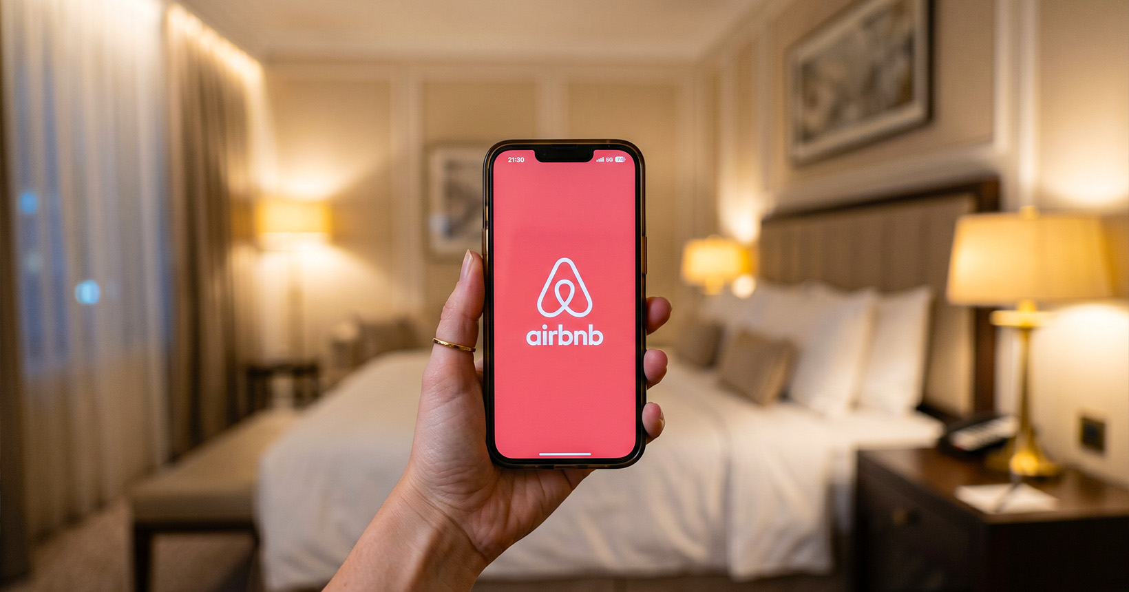 Pessoa segurando um celular com o logo do Airbnb na tela, em um quarto.
