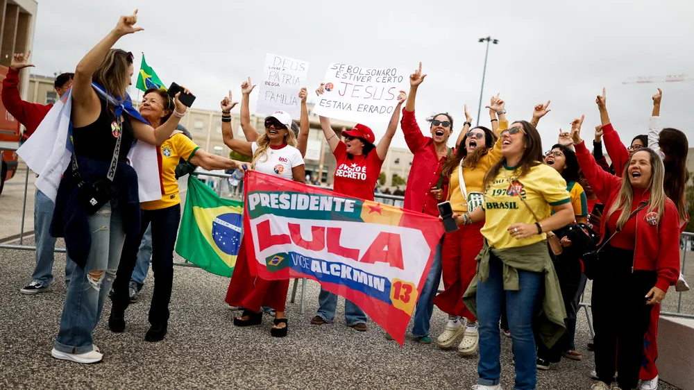 Apoiadores de Lula se reúnem com bandeiras e cartazes em local de votação de Lisboa, em Portugal.