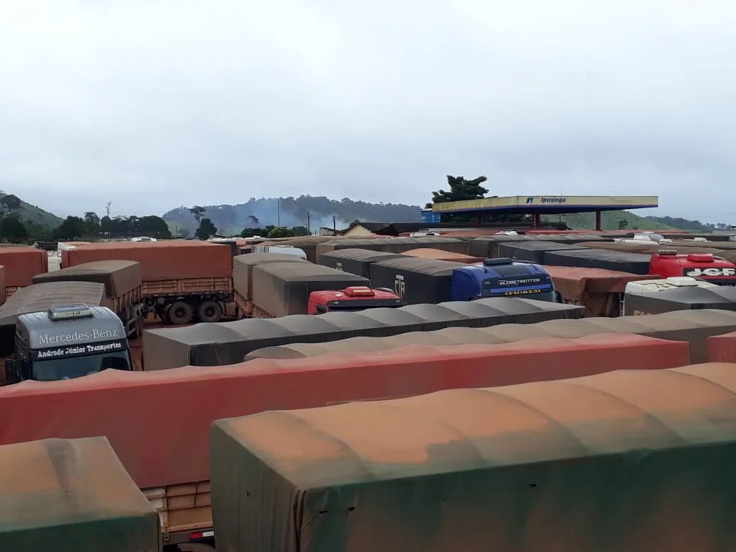 Caminhões estacionados em pátio de posto aguardando liberação da rodovia.