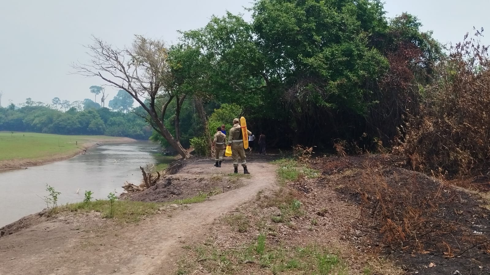 Equipes de busca em uma trilha às margens de um rio cercado por vegetação.