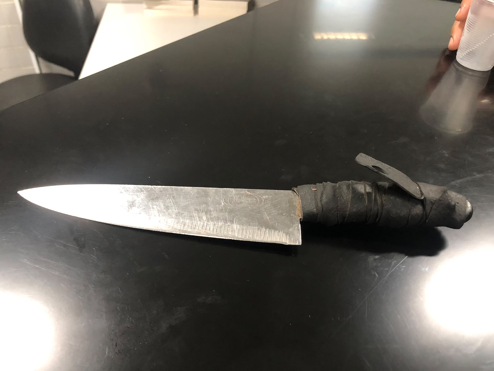 Faca com lâmina metálica e cabo escuro sobre uma mesa preta.